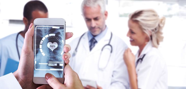 Hand holding smartphone against doctors using a tablet