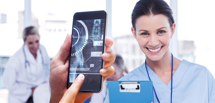 hand holding smartphone against cheerful young surgeon posing with colleagues in background