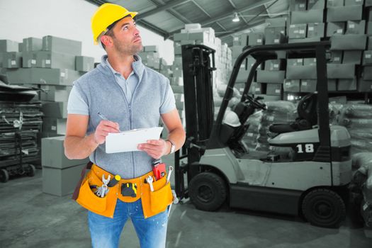 Manual worker looking away while writing on clipboard against warehouse worker loading up pallet