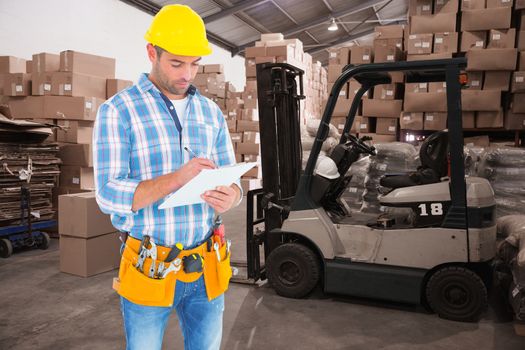 Manual worker writing on clipboard against warehouse worker loading up pallet