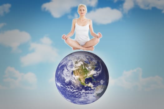 Toned young woman sitting in lotus pose with eyes closed against blue sky