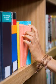 Student picking a book from shelf in library at the university