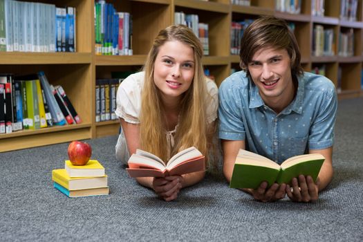 Students reading book lying on library floor at the university 