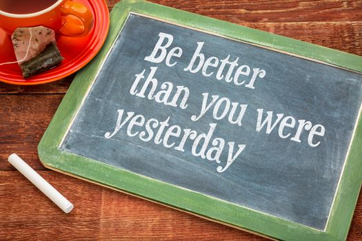Be better than you were yesterday - motivational text on a slate blackboard with chalk and cup of tea