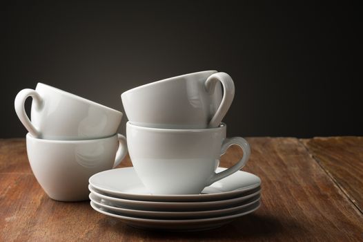 Four plain white ceramic coffee or tea cups with stacked saucers standing ready on a table in a home, cafeteria or coffee house to serve an aromatic cup of relaxing beverage