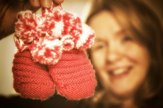 Blond woman is holding two pink baby shoes