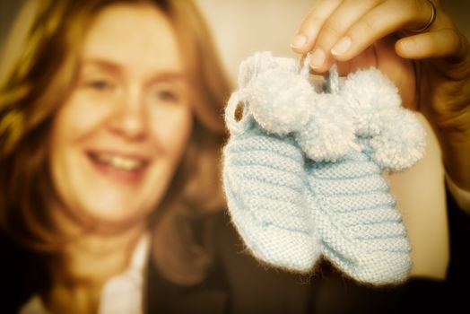 Blond woman is holding two blue baby shoes