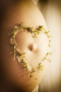 Image of a baby bump with cream cress heart in warm sun light