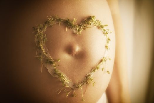 Image of a baby bump with cream cress heart in warm sun light