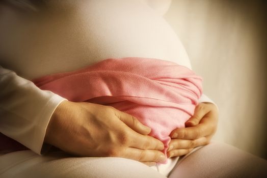 Pregnant woman in white clothes and pink scarf is holding her baby bump