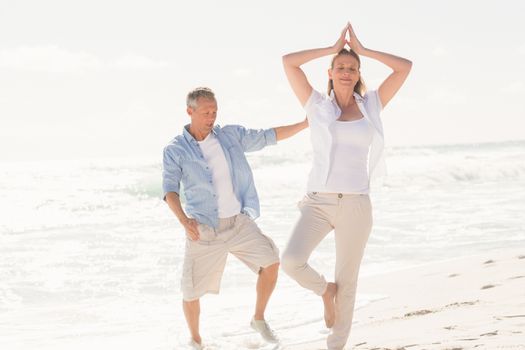 Happy couple doing yoga at the beach