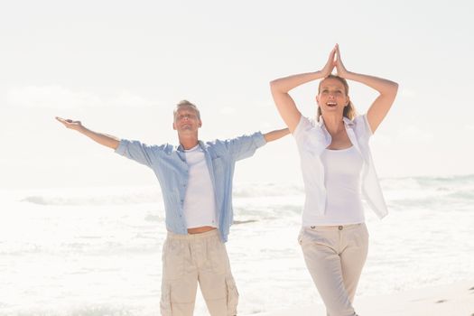 Happy couple doing yoga at the beach