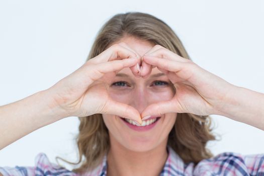Smiling hipster doing heart shape with her hands on white background 