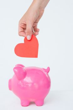 Woman holding piggy bank and red heart on white background