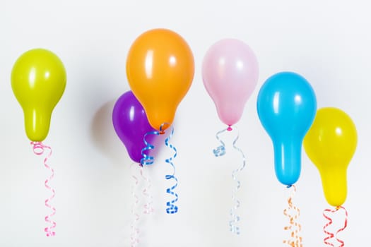 Balloons of different bright colors are hanging on a white background