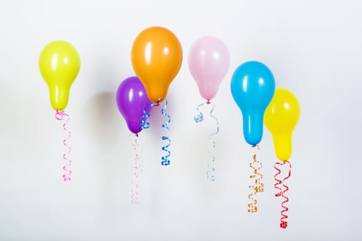Balloons of different bright colors are hanging on a white background