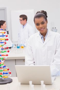 Smiling scientist using laptop while colleagues talking together in the laboratory 