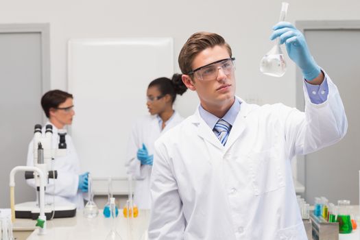 Scientist looking at white precipitate while colleagues talking together in the laboratory 