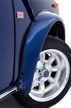 Modern new blue British car in retro style showing the front wheel arch and new spoked alloy wheel on a white background