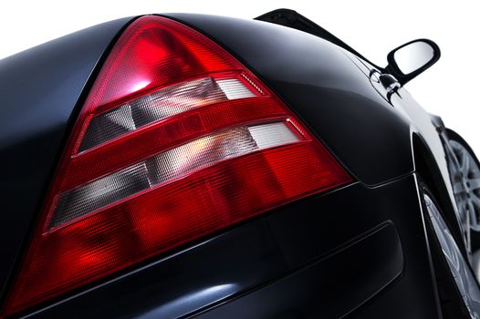 Close up low angle view of the red rear tail light assembly on a modern black car showing lens detail isolated on white