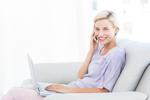 Pretty blonde woman calling on the phone and using her laptop in the living room