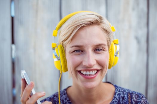 Pretty blonde woman listening music with her mobile phone on wooden background