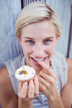 Pretty blonde woman tasting the cupcake on wooden background