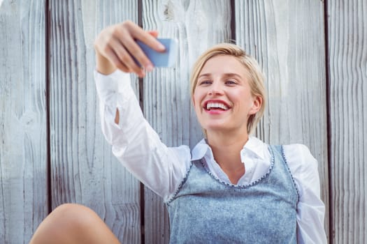 Pretty blonde woman taking selfie on wooden background