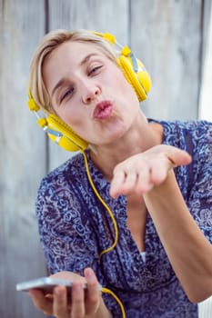 Pretty blonde woman listening music with her mobile phone and blowing kiss on wooden background