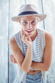 Pretty blonde woman wearing hat and smiling at camera on wooden background