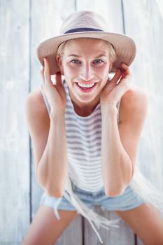 Pretty blonde woman wearing hat and smiling at camera on wooden background