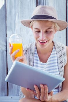 Pretty blonde woman using her tablet and holding orange juice on wooden background