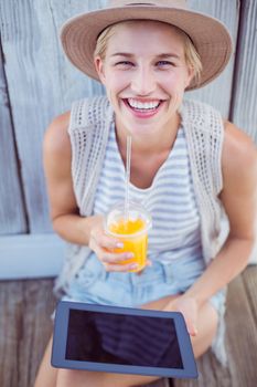 Pretty blonde woman using her tablet and holding orange juice on wooden background