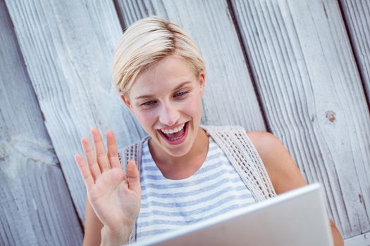 Pretty blonde woman speaking with someone online on wooden background