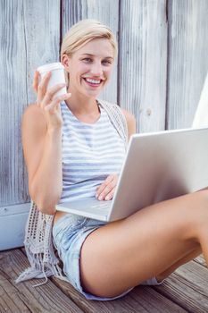 Pretty blonde woman using her laptop and drinking coffee on wooden background