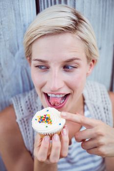 Pretty blonde woman tasting the cupcake on wooden background