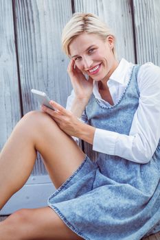 Pretty blonde texting with her mobile phone on wooden background