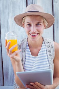 Pretty blonde woman using her tablet and holding orange juice on wooden background