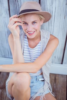 Pretty blonde woman wearing hat and smiling at camera on wooden background