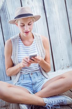 Pretty blonde woman texting with her mobile phone on wooden background 