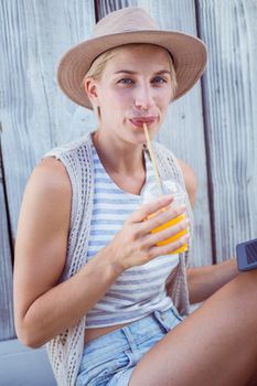 Pretty blonde woman using her tablet and drinking orange juice on wooden background