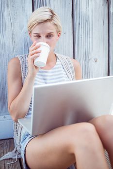 Pretty blonde woman using her laptop and drinking coffee on wooden background