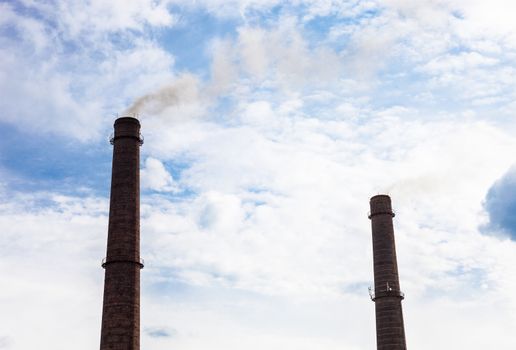Two smoke stacks of the industrial plant against the cloudy sky