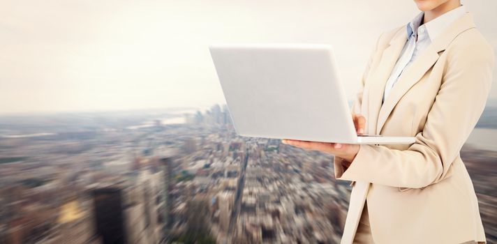 Confident businesswoman holding laptop against new york
