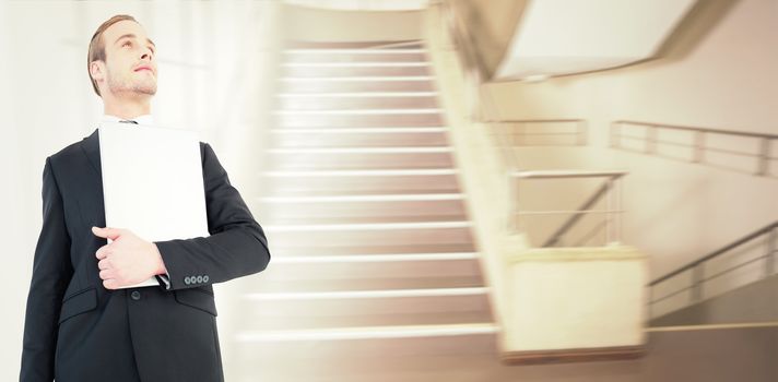 Businessman looking up holding laptop against empty stair way 