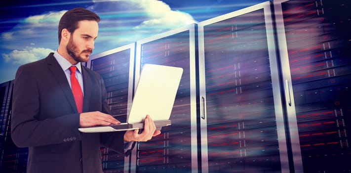 Focused businessman using his laptop against composite image of server towers