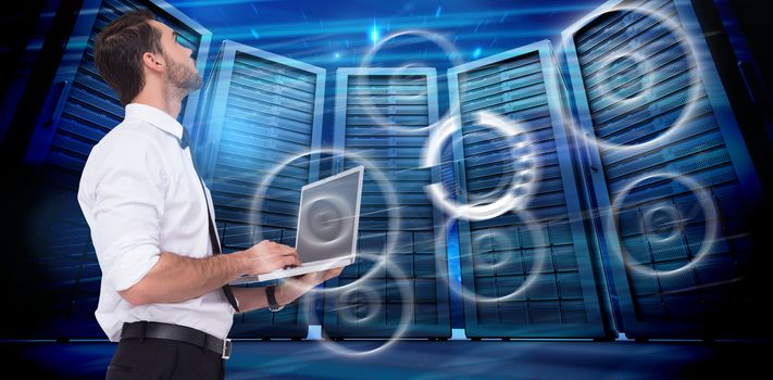 Sophisticated businessman standing using a laptop  against composite image of server room