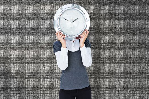 Woman holding clock in front of her head  against grey background
