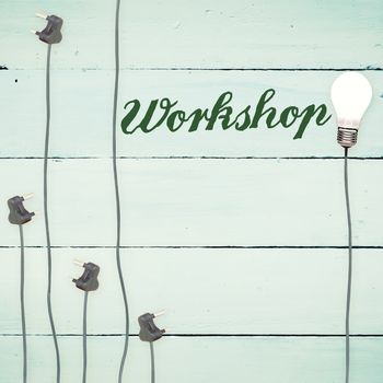 The word workshop against light bulbs on wooden background