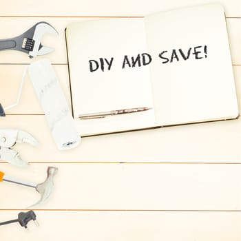 The word diy and save! against tools and notepad on wooden background